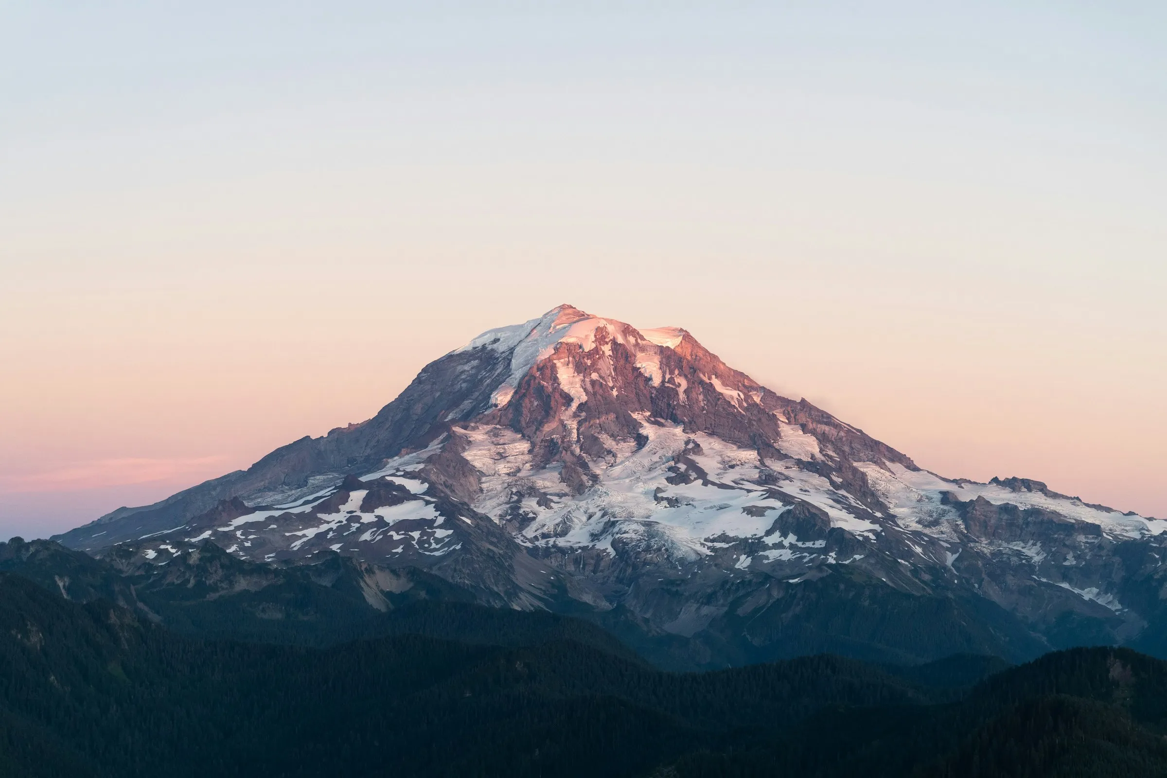 Mount Rainier glowing pink at sunset above forested ridges